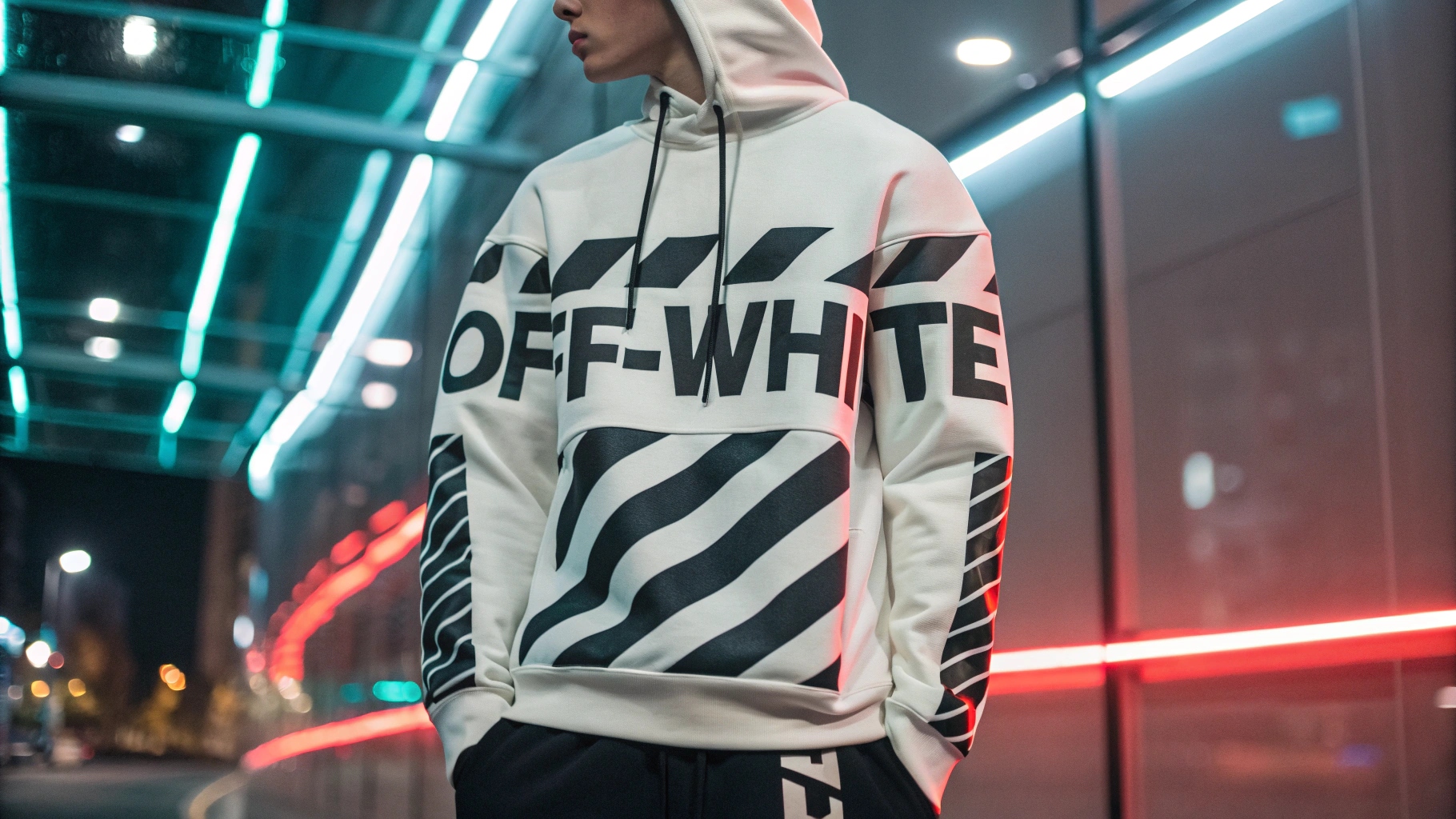 A model wearing a custom-designed Off-White-inspired hoodie with bold typography, diagonal stripe patterns, and industrial-style detailing, paired with tapered joggers, set against a futuristic urban backdrop with neon reflections, highlighting exclusivity and luxury craftsmanship.